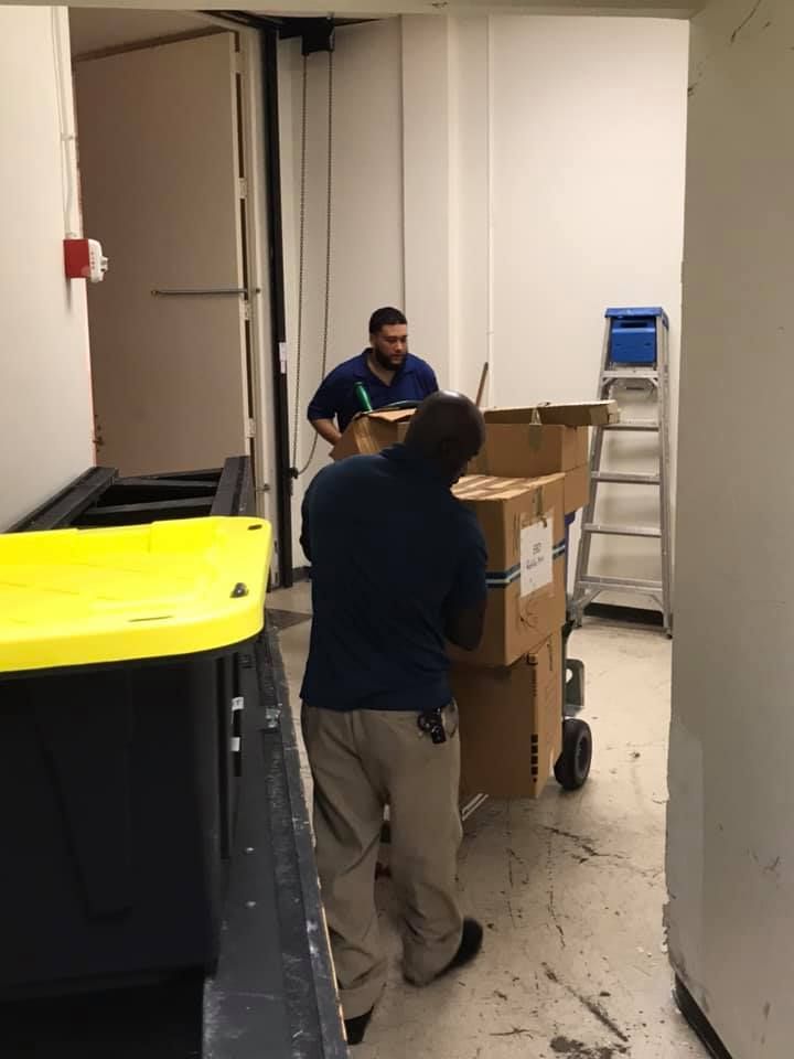 Two men are moving boxes on a cart in a room. 28.4845° N, 81.2519° W