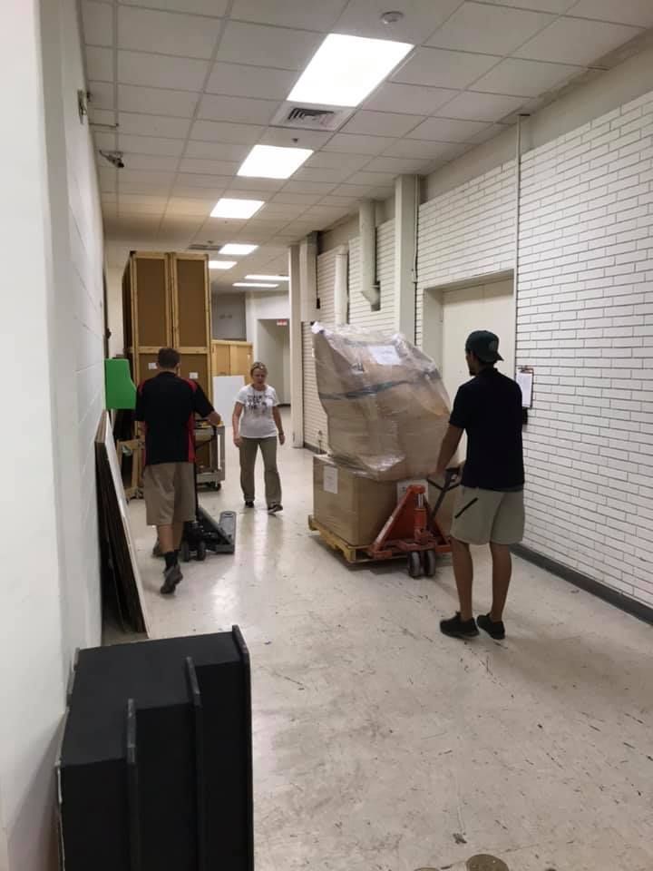 A group of people are moving a large box down a hallway. 28.4845° N, 81.2519° W