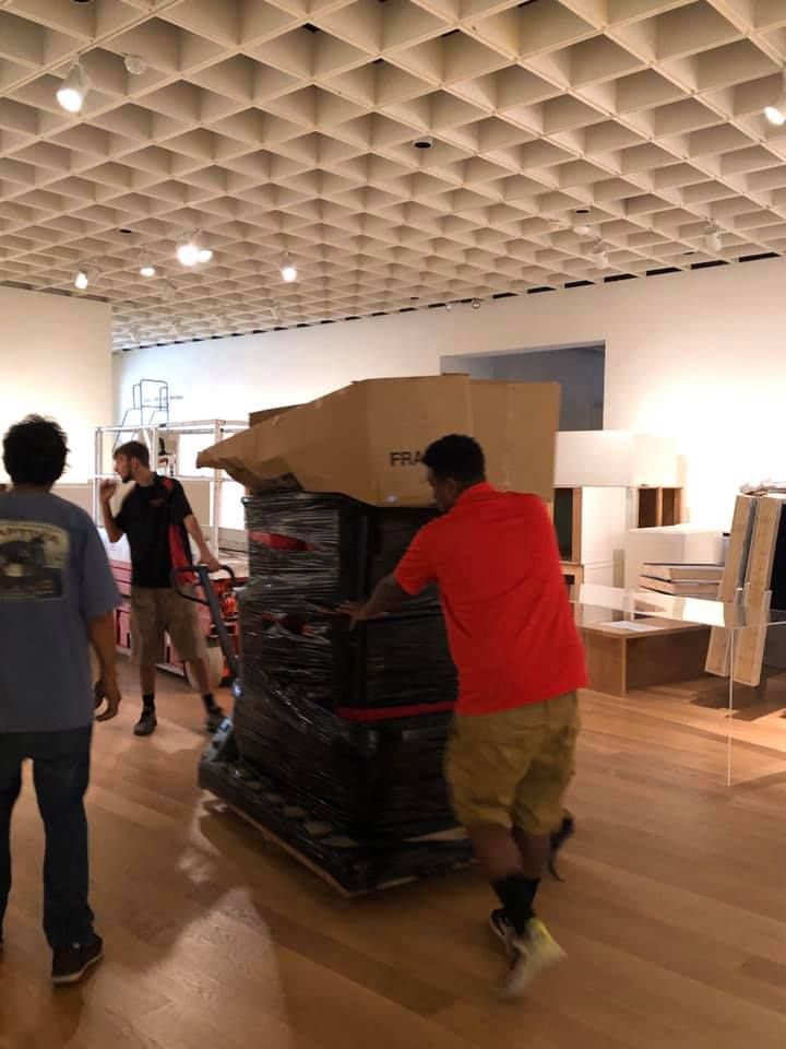 A man in a red shirt is pushing a large box on a cart. 28.4845° N, 81.2519° W