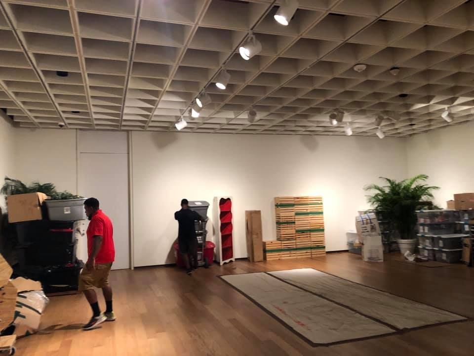A man in a red shirt is standing in a room with boxes on the floor