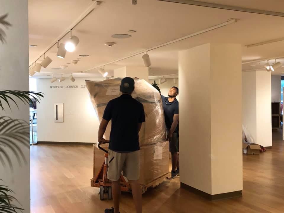 Two men are moving a large box on a dolly in a room. 28.4845° N, 81.2519° W