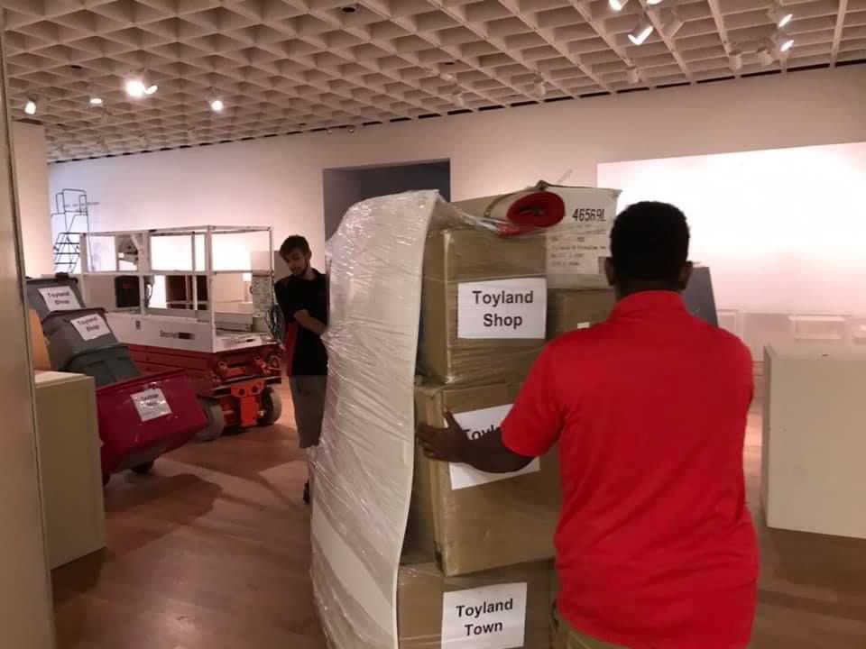 A man in a red shirt is carrying boxes in a room. 28.4845° N, 81.2519° W