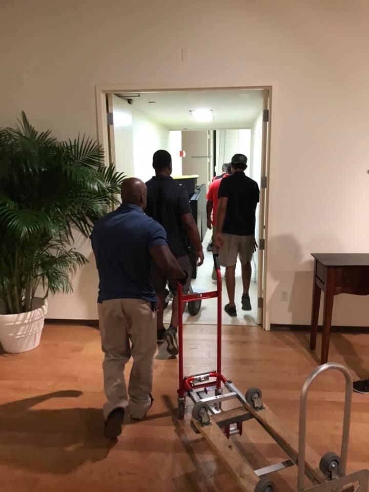 A group of men are pushing a dolly through a doorway. 28.4845° N, 81.2519° W