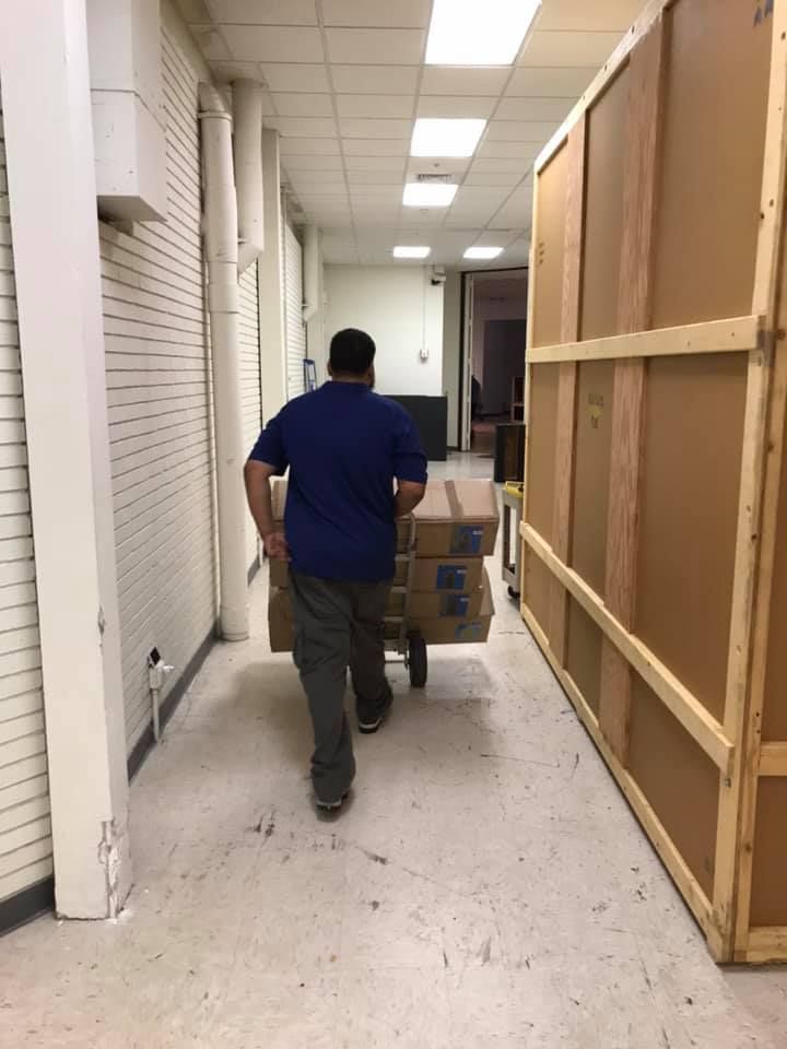 A man is pushing a cart full of boxes down a hallway. 28.4845° N, 81.2519° W