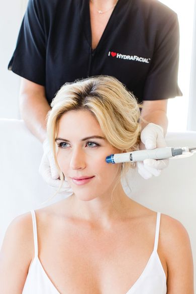 Eine Fachkraft führt eine HydraFacial-Behandlung am Gesicht einer Person mit einem speziellen Handgerät durch.