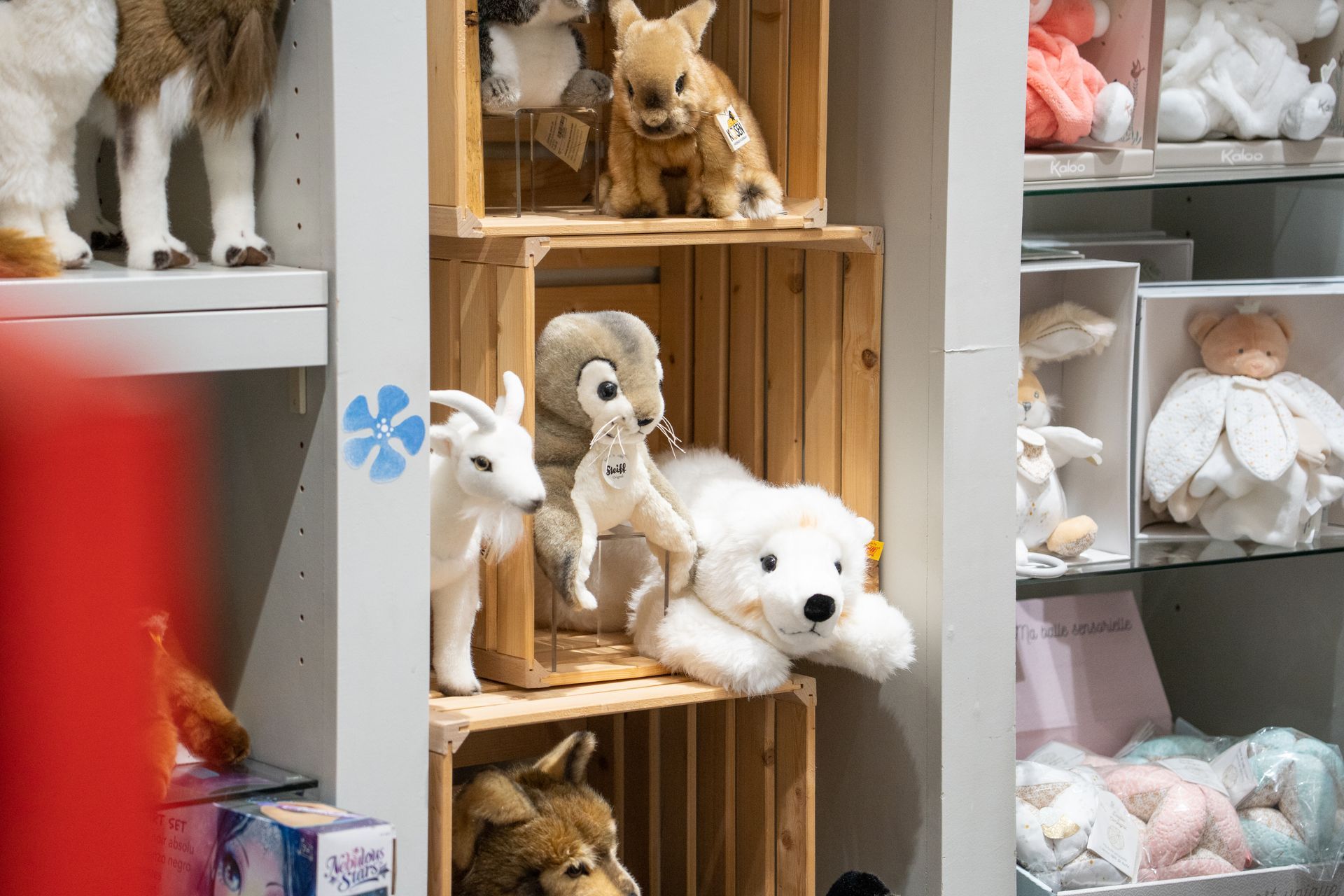 Plüschtiere, darunter ein Hase, eine Ziege und ein Bär, sind in einem Ladenauslage auf Holzregalen arrangiert.