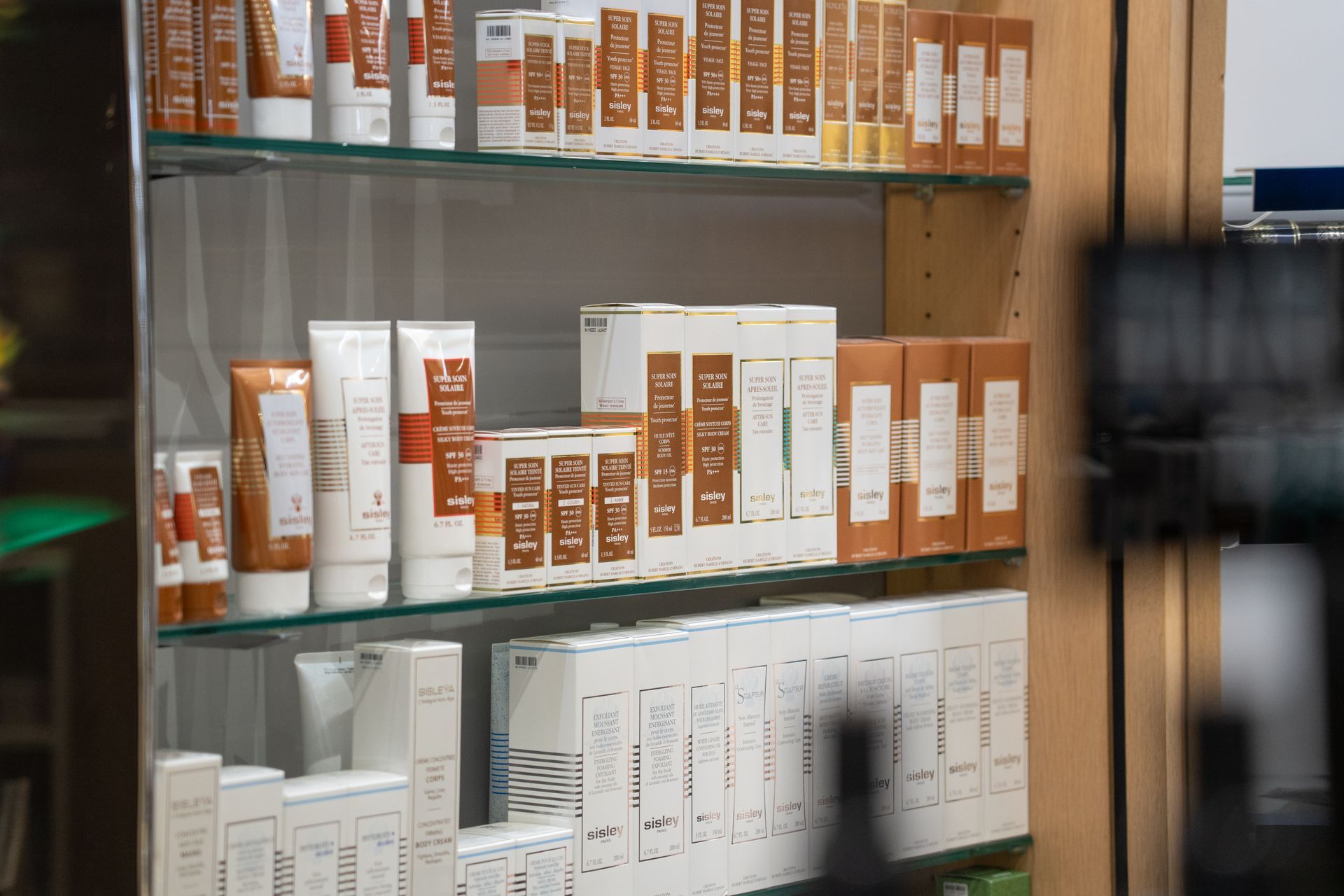 Ladenregal mit weissen und bronzefarbenen Hautpflegeprodukten: Tuben, Flaschen und Schachteln in eleganter Präsentation.