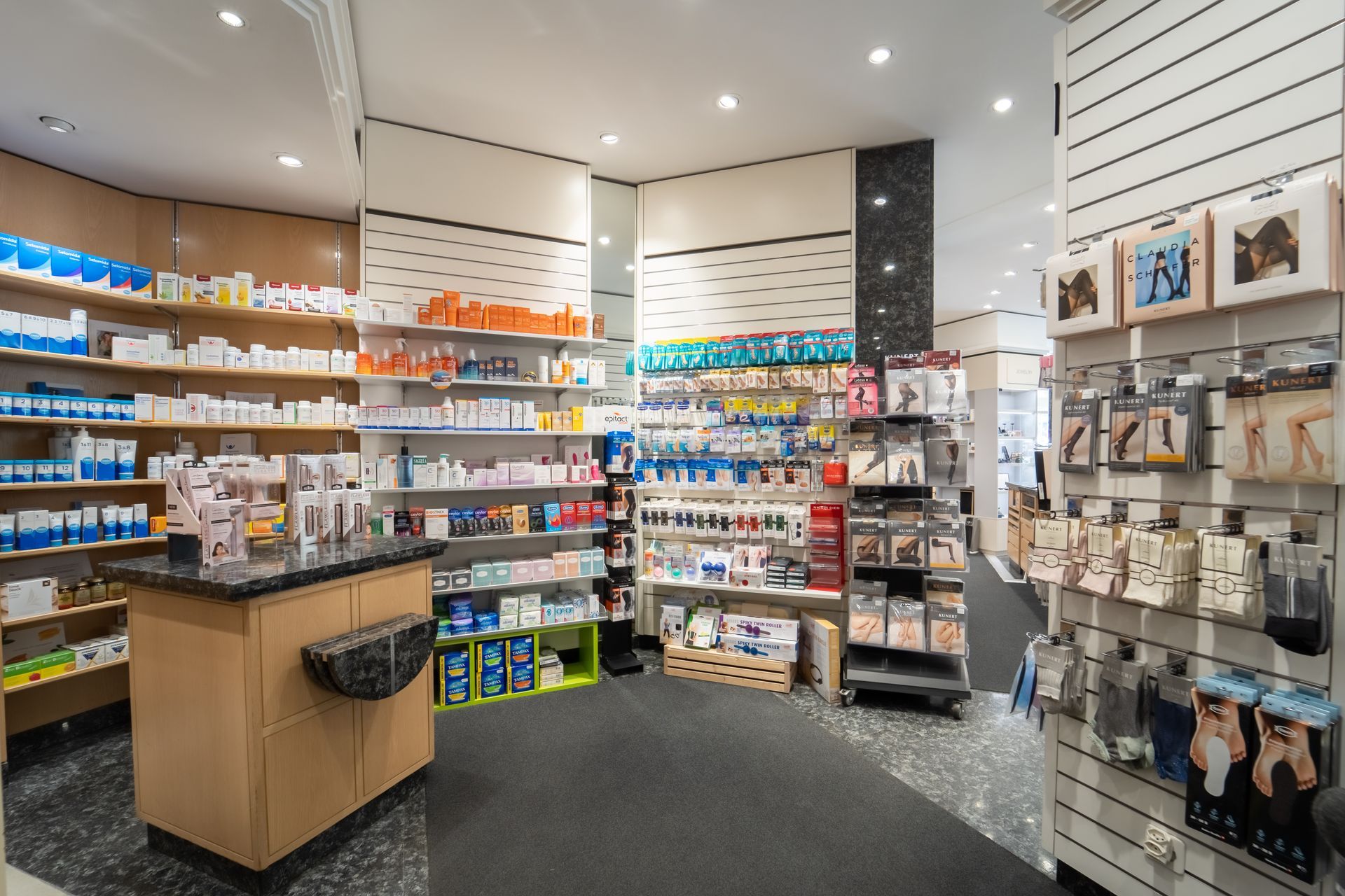 Innenansicht einer gut beleuchteten Apotheke mit Regalen voller medizinischer Artikel, Gesundheitsprodukte und Strumpfwaren.