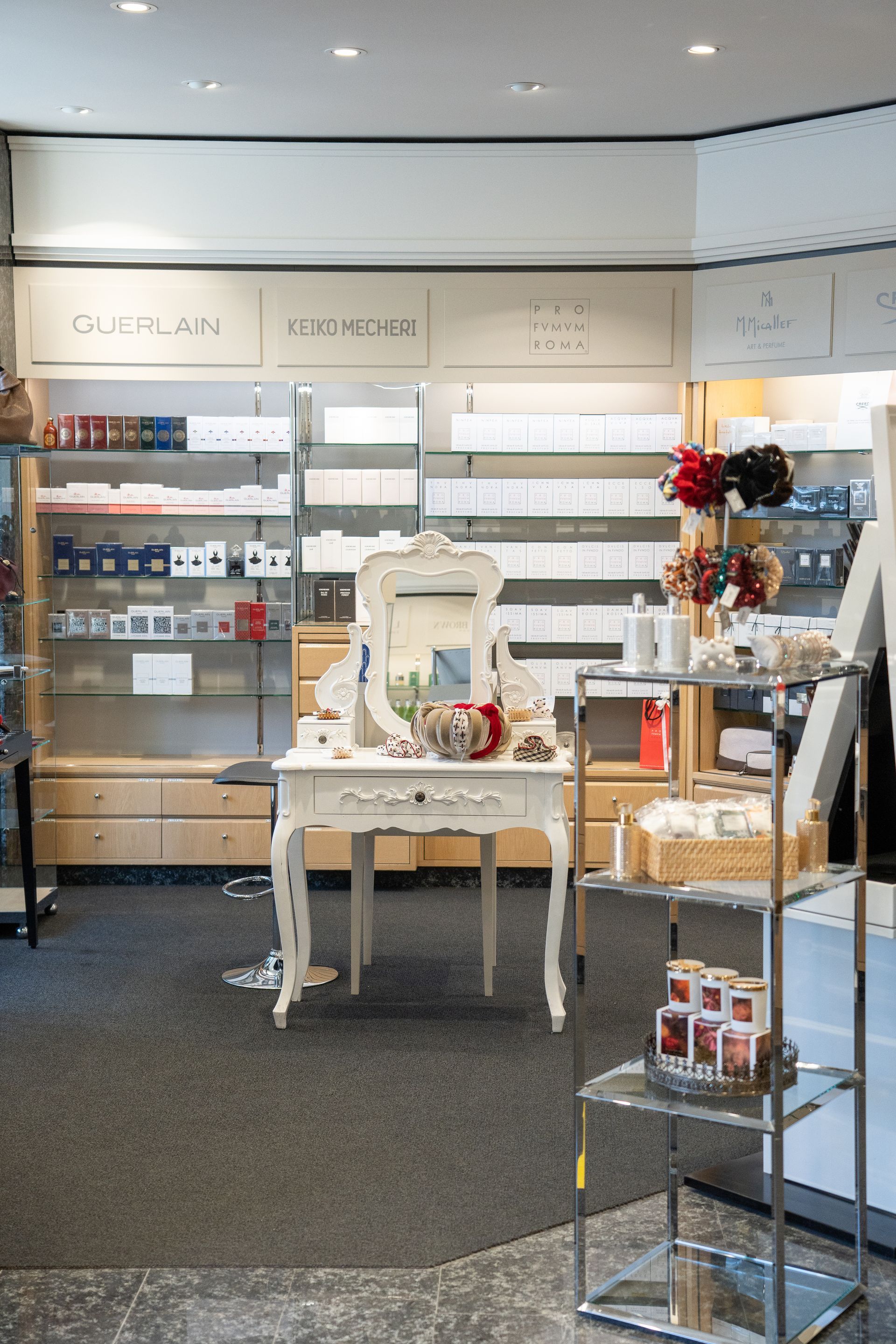 Schönheitssalon-Interieur: weisser Schminktisch mit Spiegel, Holzregale mit Produkten und Kleiderständer, helle Atmosphäre.