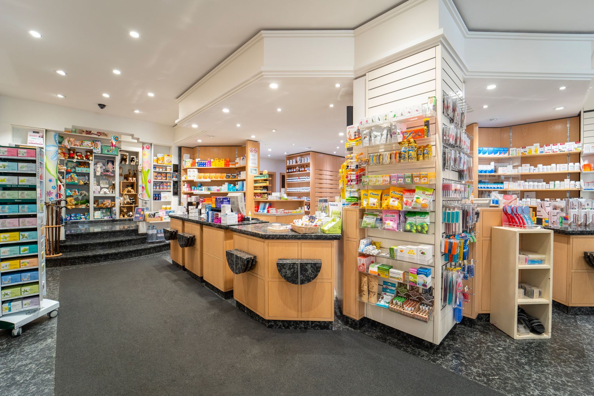 Ein helles Apothekeninterieur mit Regalen voller Produkte, einem Bedientresen und Produktpräsentationsständern.