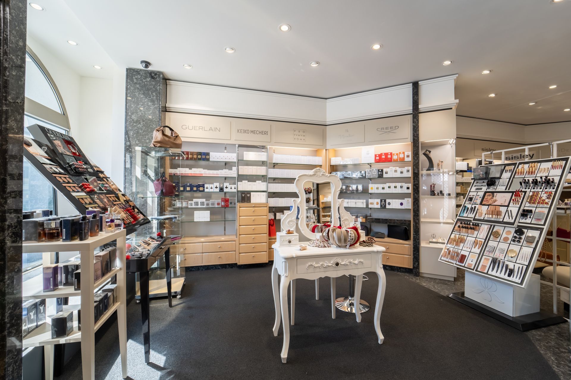 Innenansicht eines Kosmetikgeschäfts mit Warenauslagen, Regalen und einem weissen Schminktisch.