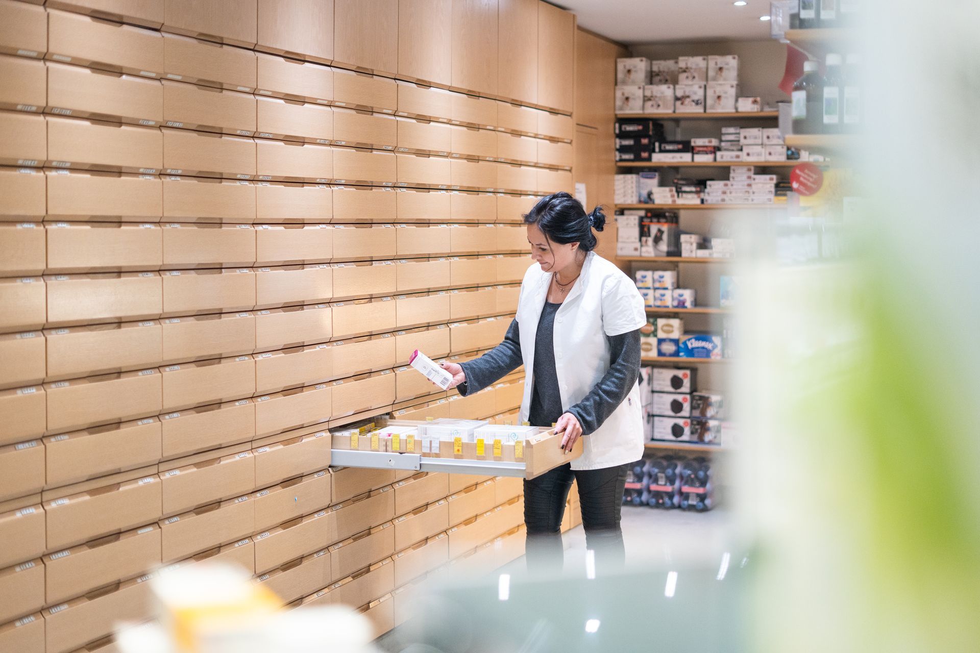 Ein Apotheker im weissen Kittel zieht in einer Apotheke eine Medikamentenschublade aus einem Wandschrank.