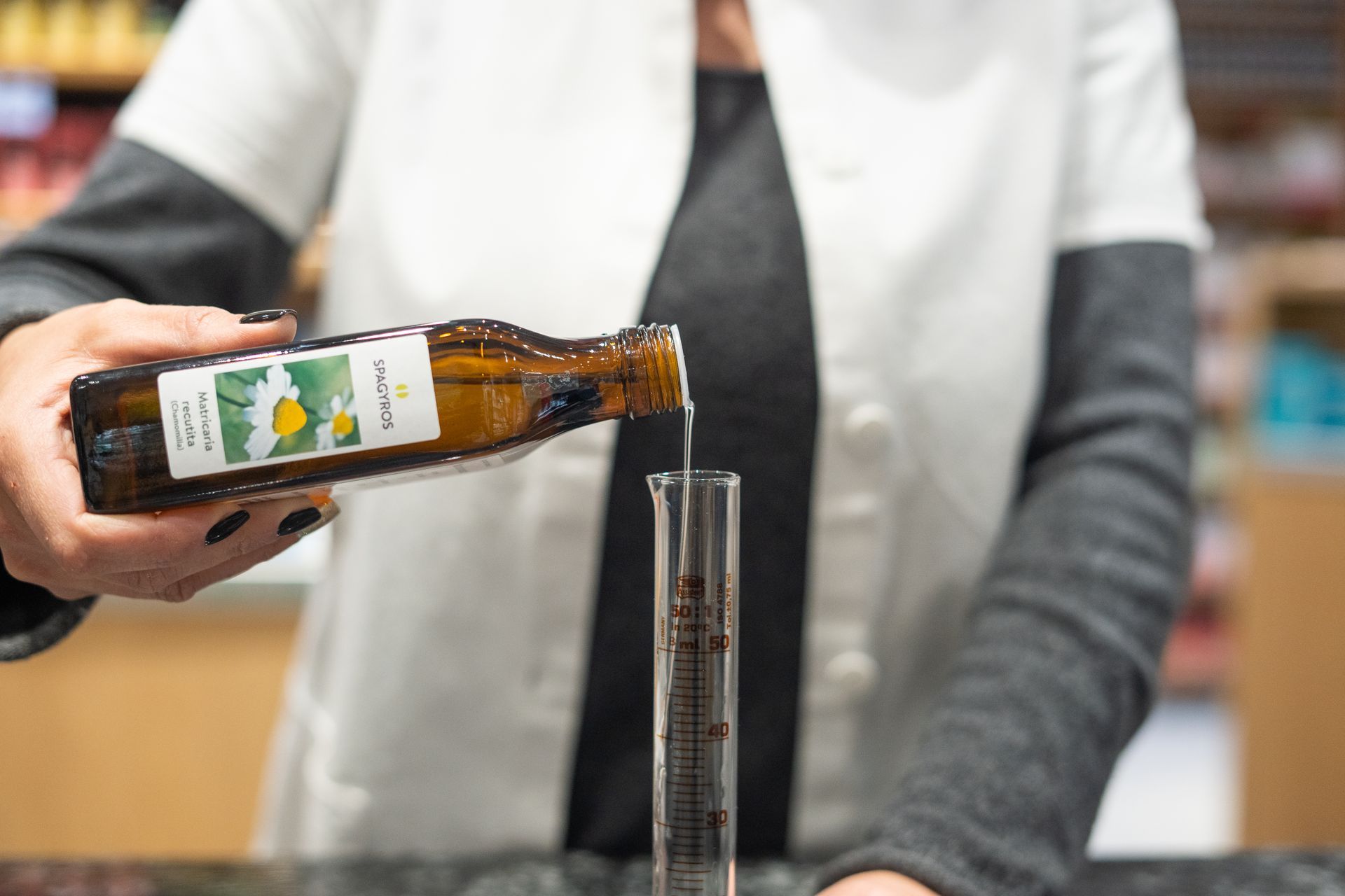 Person giesst bernsteinfarbene Flüssigkeit aus Flasche in Messzylinder, Apotheken-Labor, präzise pharmazeutische Tätigkeit.