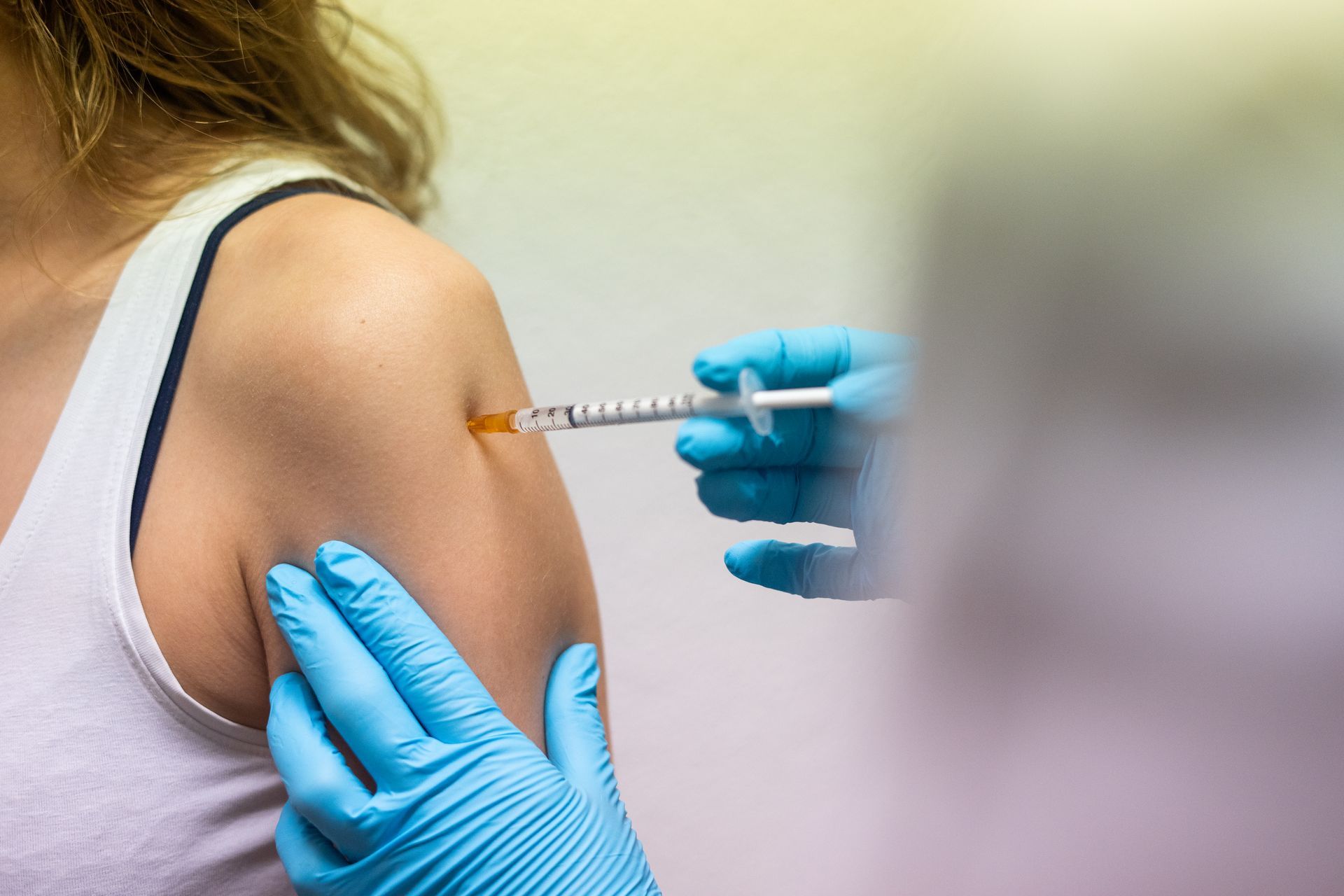 Eine medizinische Fachkraft in blauen medizinischen Handschuhen verabreicht einer Person eine Injektion in den Oberarm.