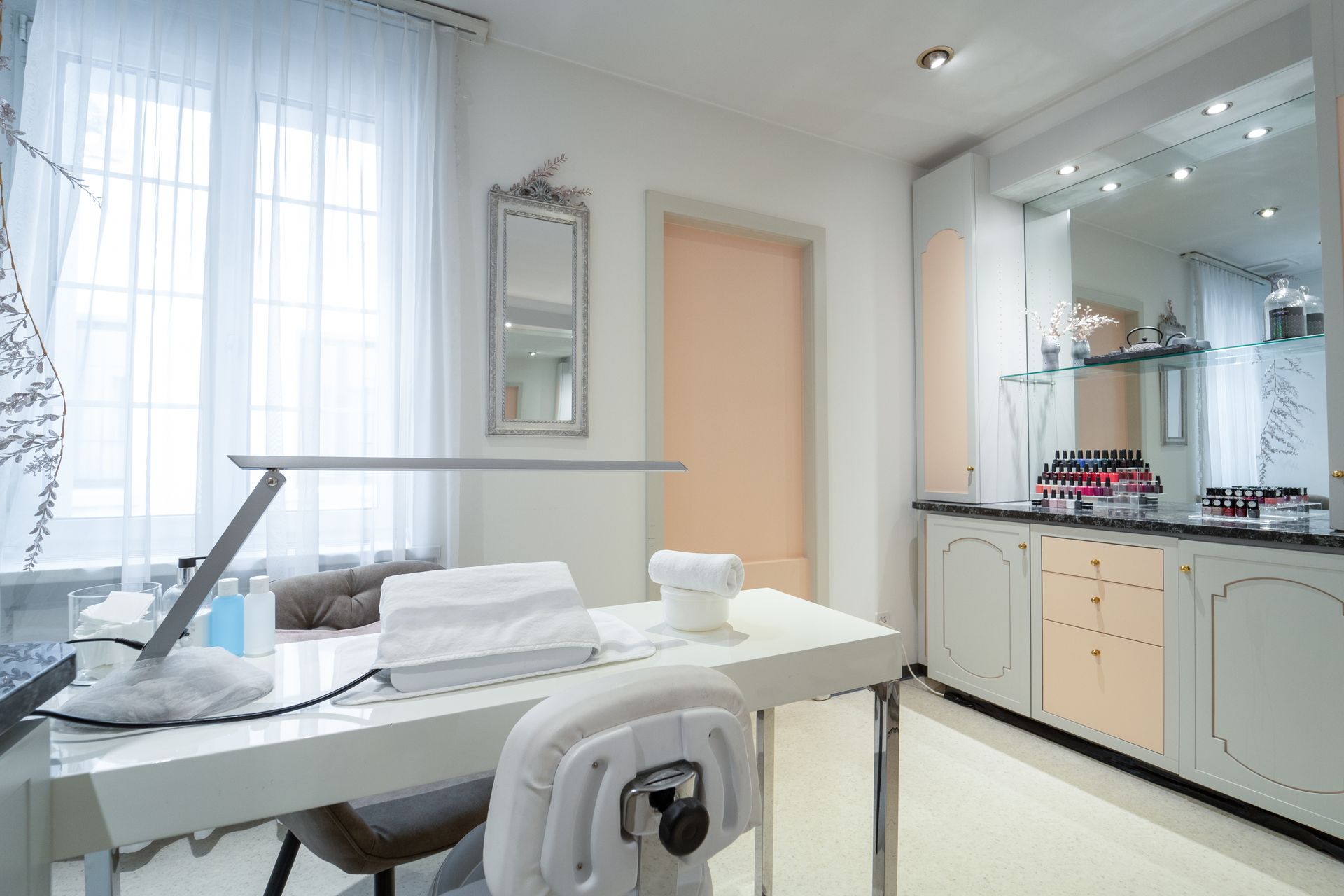 Ein heller, moderner Maniküreplatz mit weissem Schreibtisch, Stuhl, Lampe und Schränken in einem Schönheitssalon.