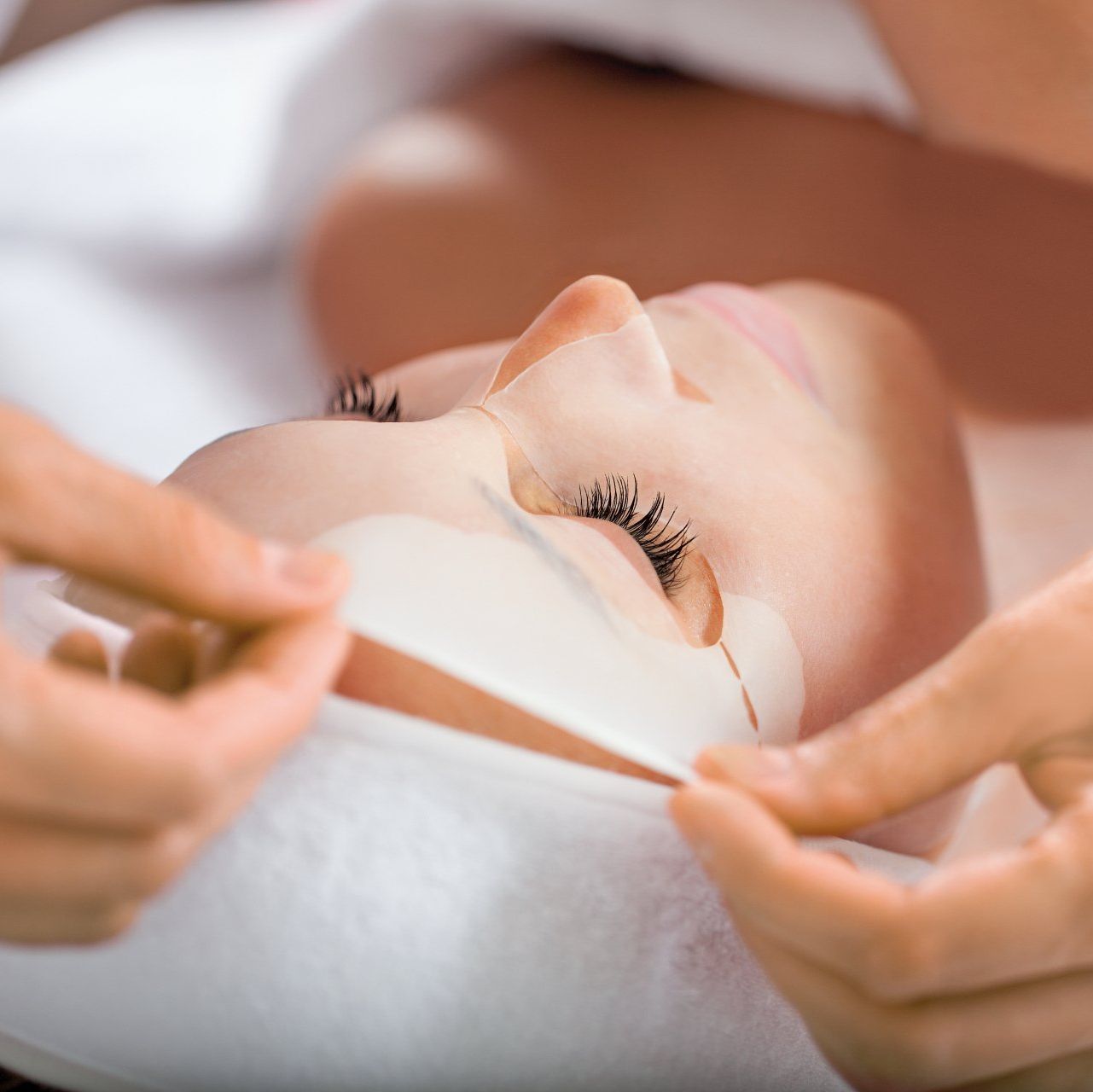 Person klebt weissen Klebestreifen unter die Augen einer Kundin während Gesichtsbehandlung, professionelle Kosmetikanwendung.