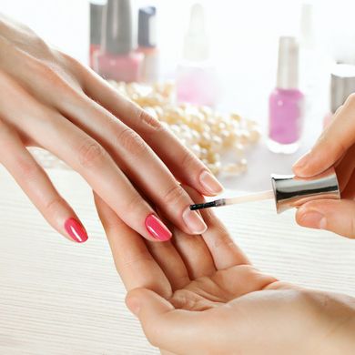 Maniküristin trägt klaren Überlack auf Fingernagel einer Kundin auf, bunte Nagellackfläschchen daneben, Nagelpflegeservice.