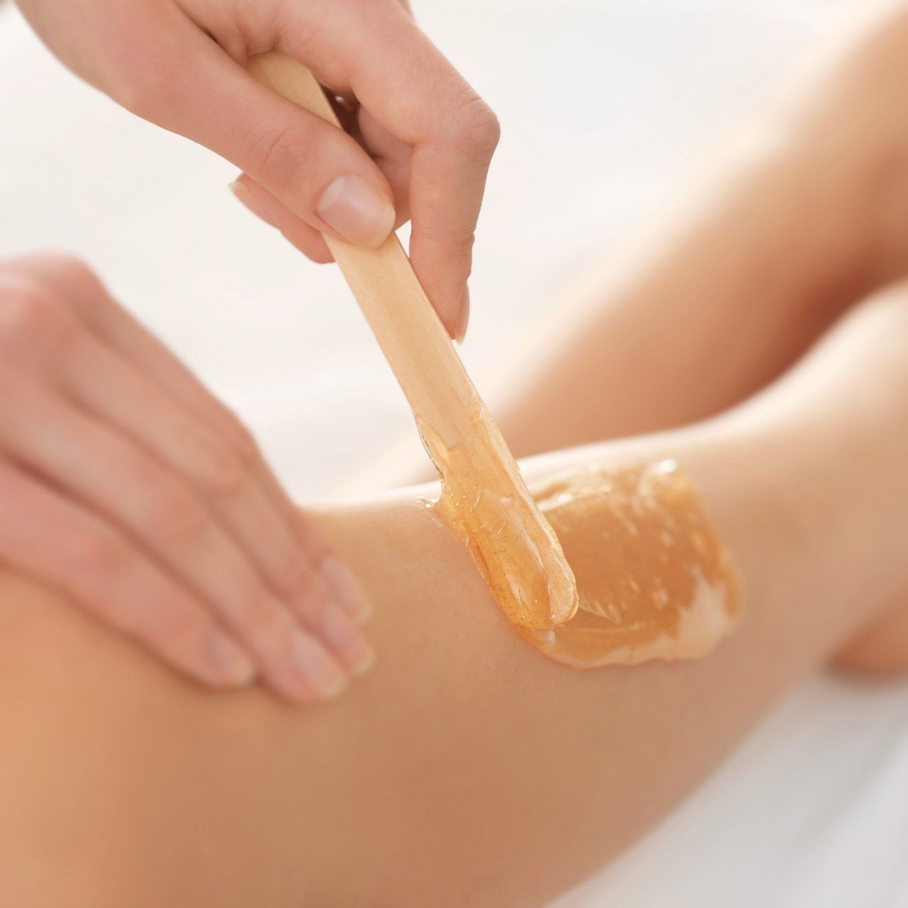 Nahaufnahme eines Holzspatels, mit dem goldenes Enthaarungswachs auf ein Bein aufgetragen wird.