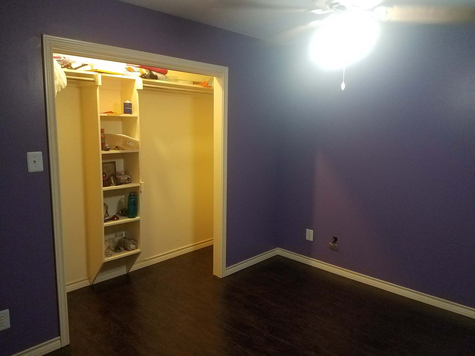 Room with purple walls, dark wood floor, open closet with shelves, and a ceiling fan.