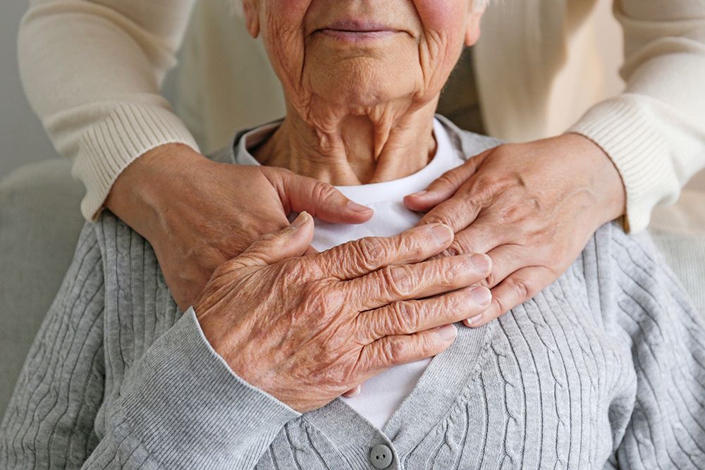 A nurse is holding the hand of an elderly woman in a wheelchair.