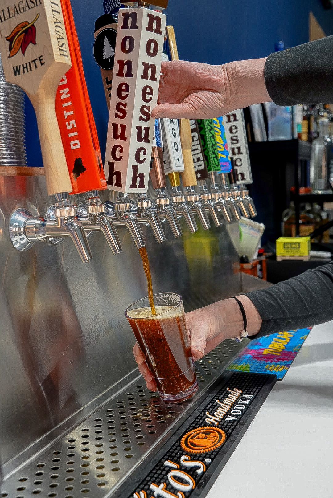 Dog licks ice cream cone held by a person against a light blue sky. Black and white dog, pink ice cream.