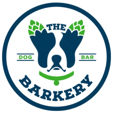 Logo for "The Barkery": a dog-shaped design with hops, collar, and text inside a blue circle.