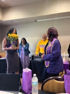 A woman in a purple jacket is holding a vase of flowers in a room.