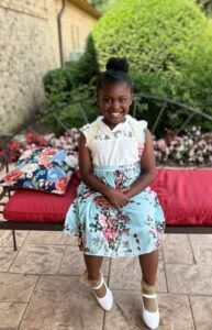 A little girl is sitting on a bench wearing a floral skirt and white shoes.