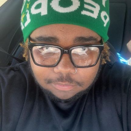 A man wearing glasses and a green beanie is sitting in a car.