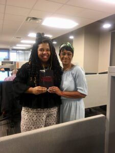 Two women are standing next to each other in an office holding a book.