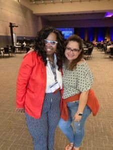 Two women are posing for a picture in a large room.