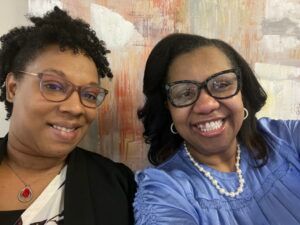 Two women wearing glasses and pearls are posing for a selfie.