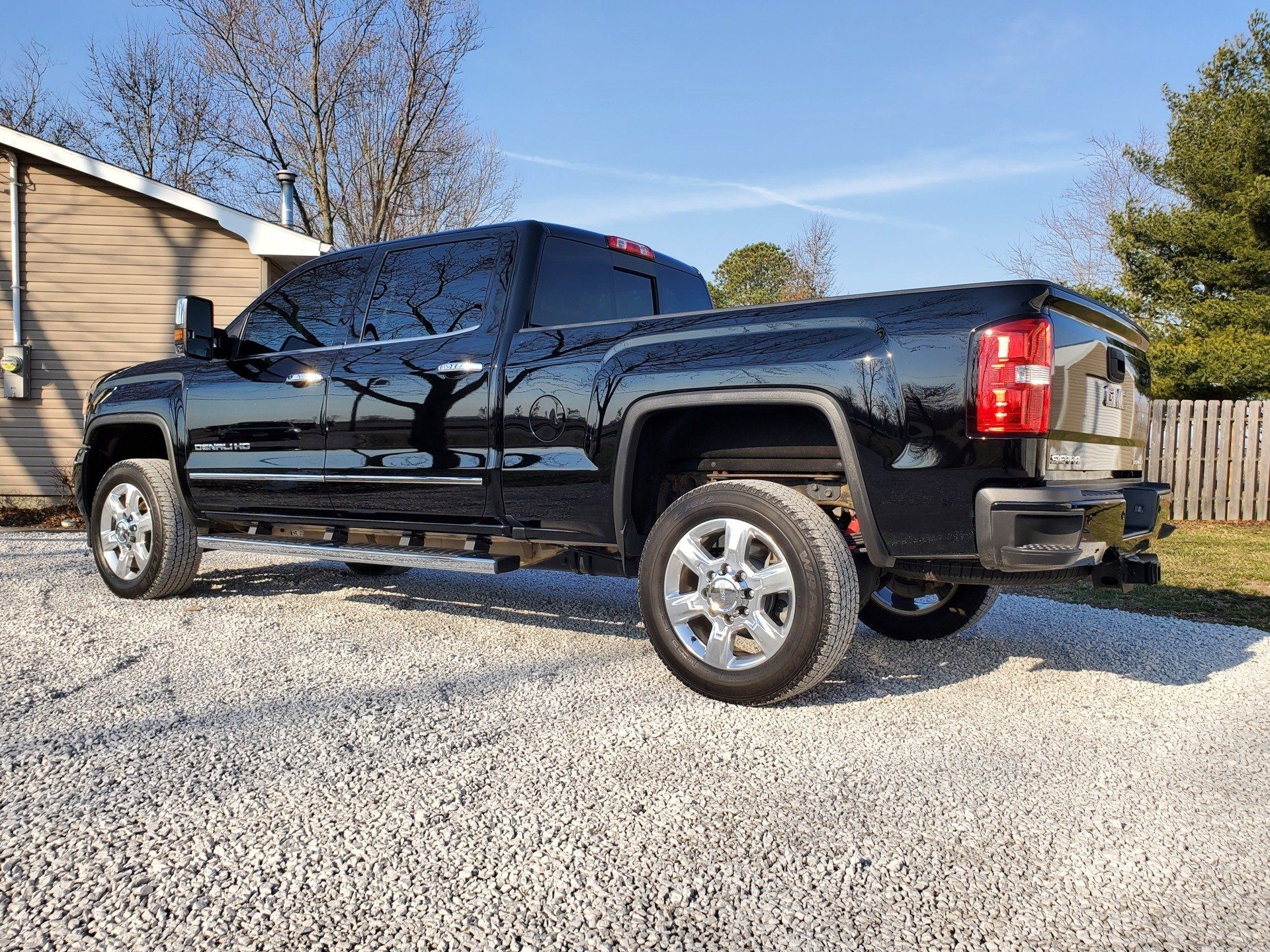 A black truck is parked on gravel in front of a house.