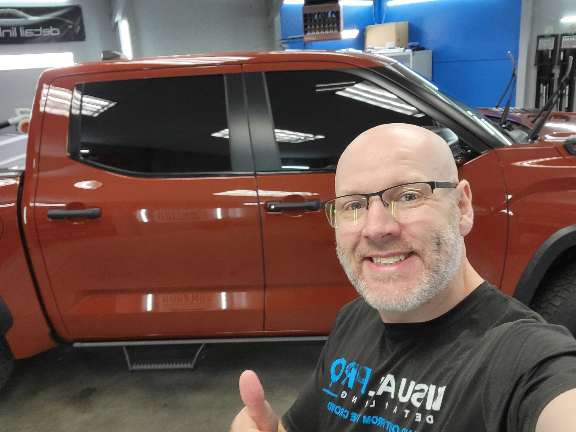 A man wearing glasses is giving a thumbs up in front of a red truck