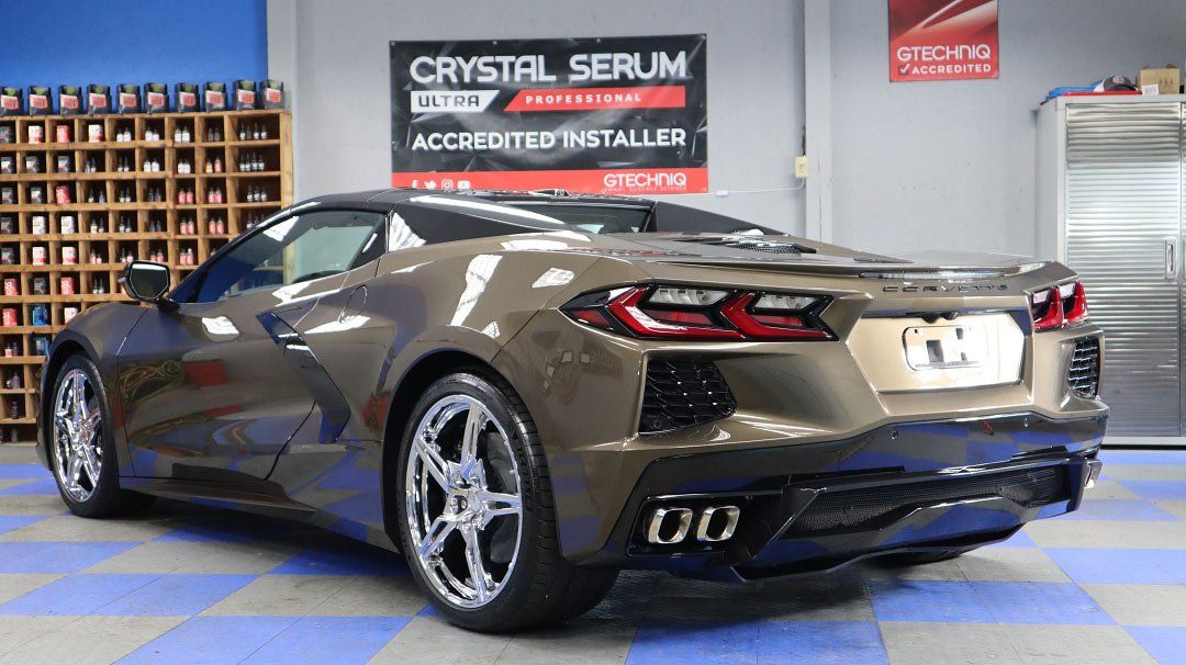 A brown sports car is parked in a garage next to a sign that says crystal serum.