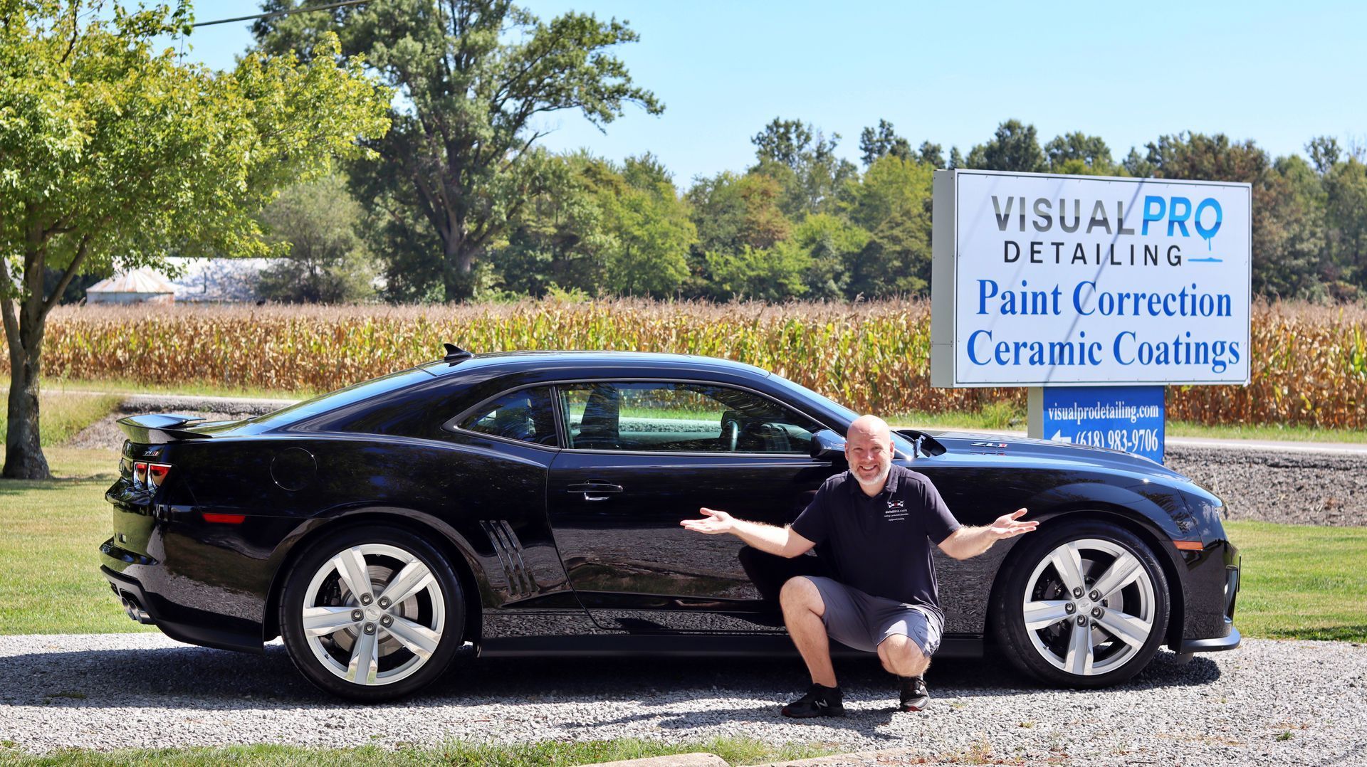 A man is kneeling next to a black car in front of a sign.