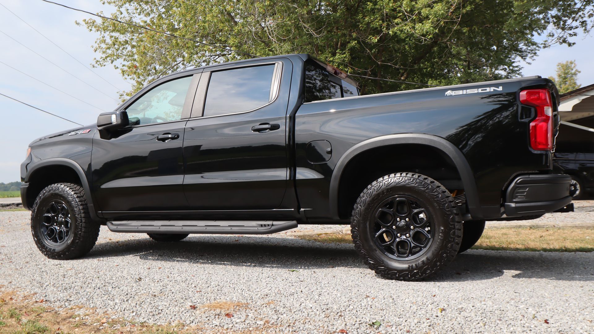 A black Chevrolet Silverado crew cab pickup truck parked on a gravel driveway outdoors.