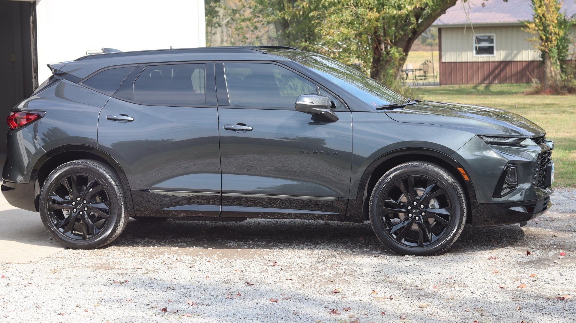 A black chevrolet blazer is parked in a gravel lot in front of a house.
