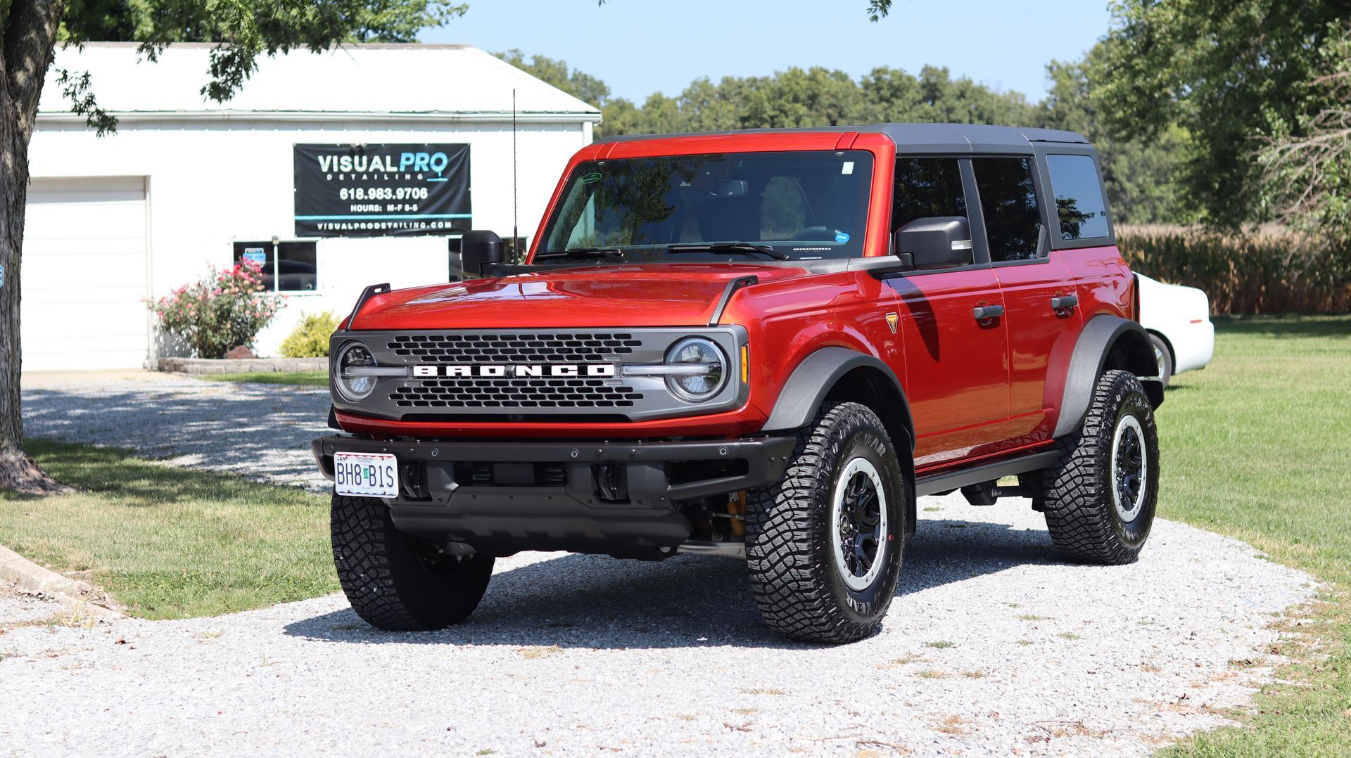 A red ford bronco is parked on a gravel road in front of a building.