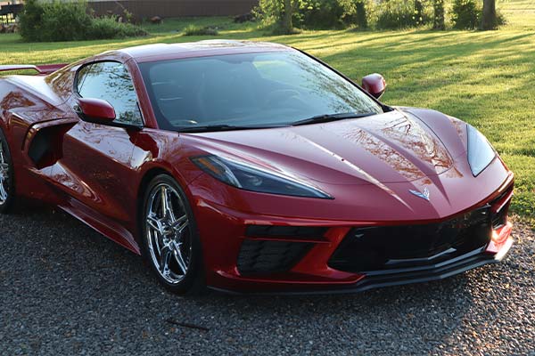 A red sports car is parked in a gravel driveway.