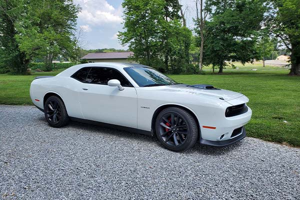 A white dodge challenger is parked on a gravel road.