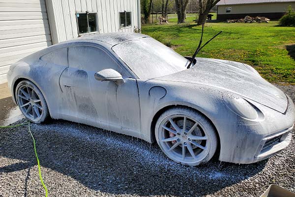 A porsche 911 is covered in foam in a driveway.