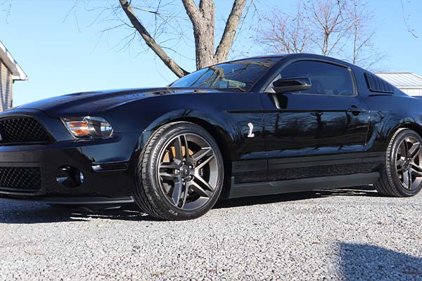 An orange sports car is parked in front of a paint correction ceramic center sign.