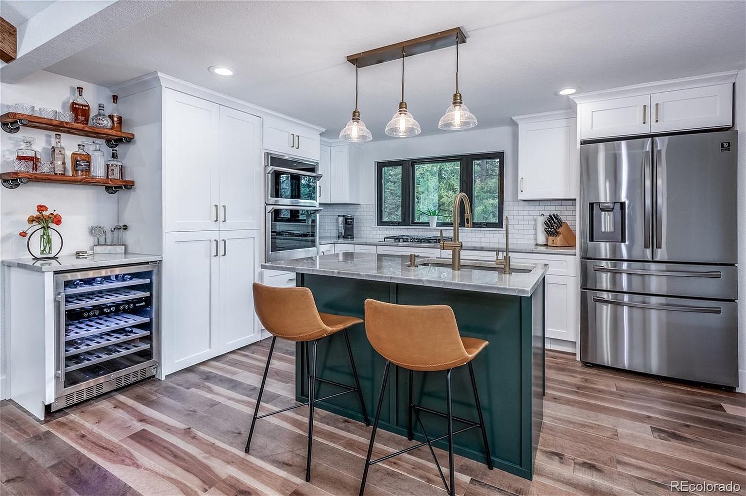 A kitchen with stainless steel appliances , a wine cooler , a refrigerator and a bar.