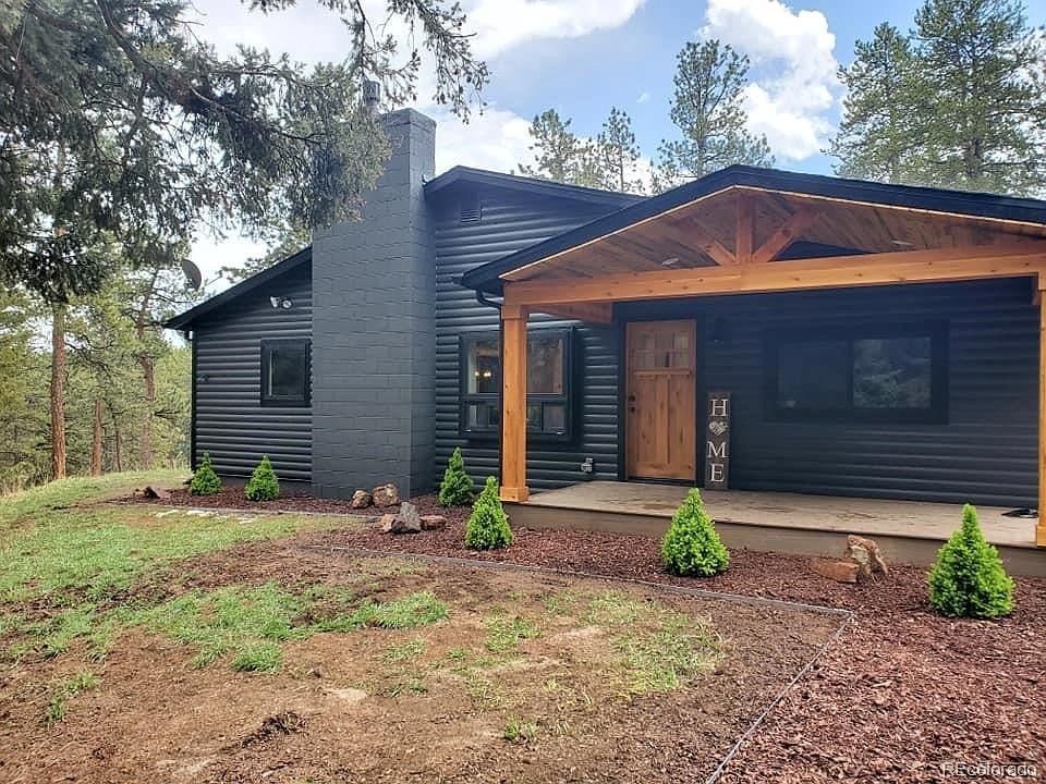 A black house with a wooden porch and a sign that says `` home ''.