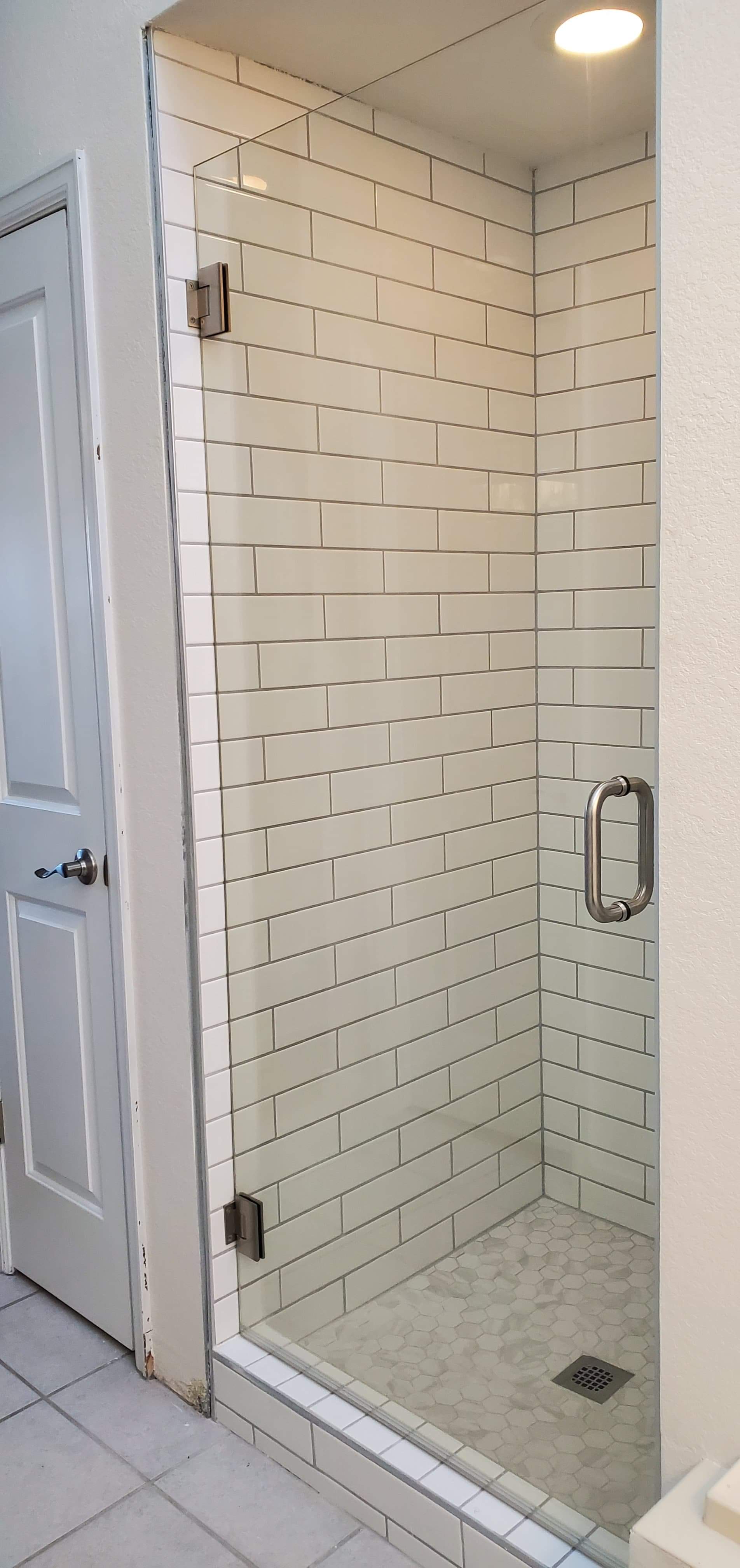 A bathroom with a walk in shower with white tiles and a glass door.