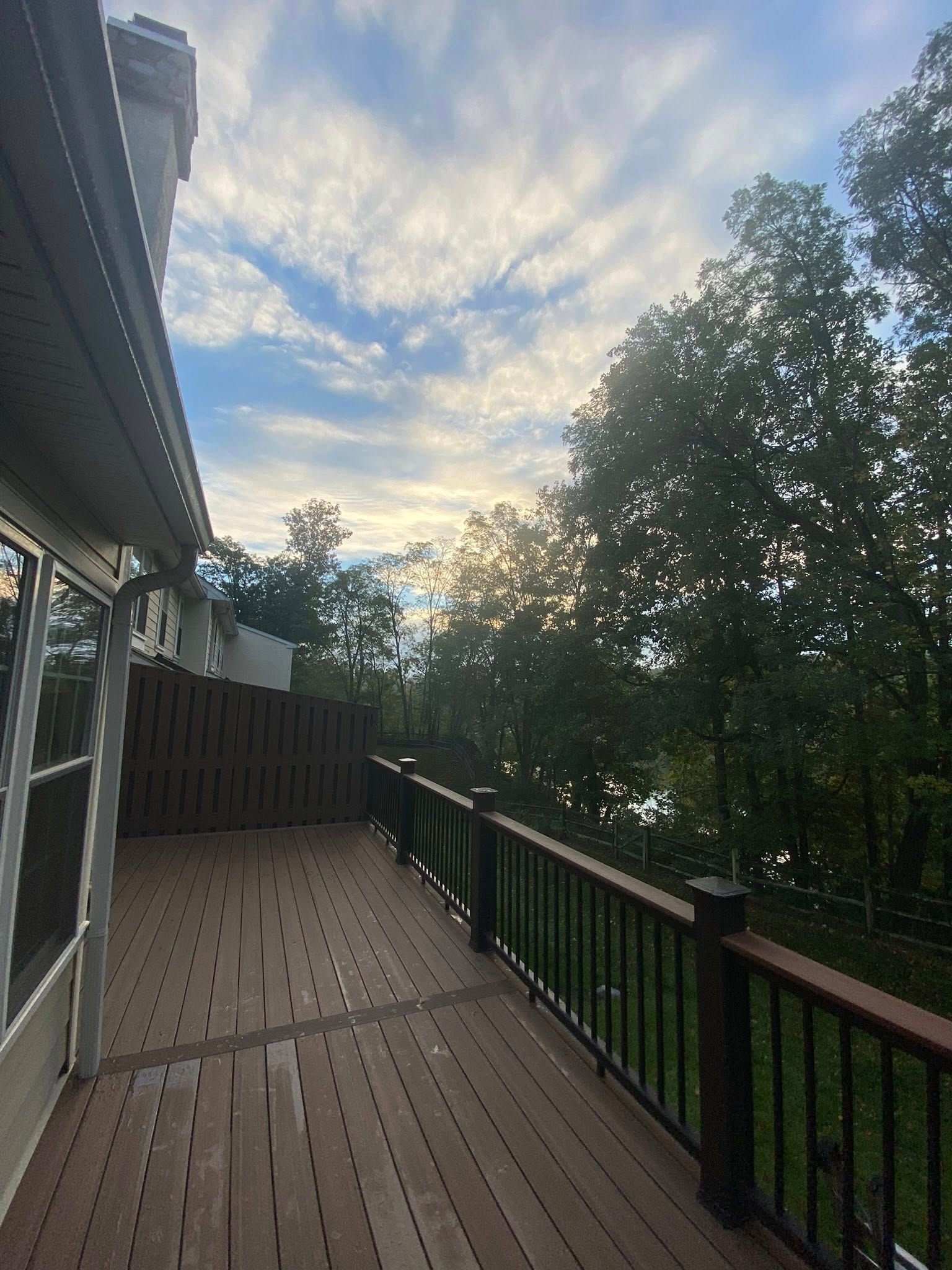 Wooden deck overlooking trees at sunset, with a cloudy sky and railing along the side.