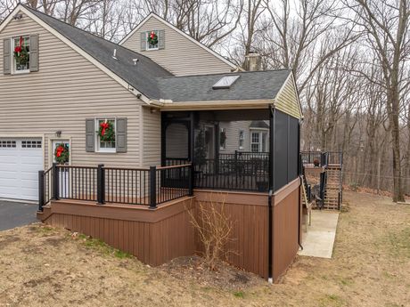 Tan house with a brown deck and screened porch beside a wooded yard
