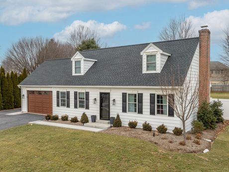 White suburban house with gray roof, brick garage, and front lawn under a clear sky