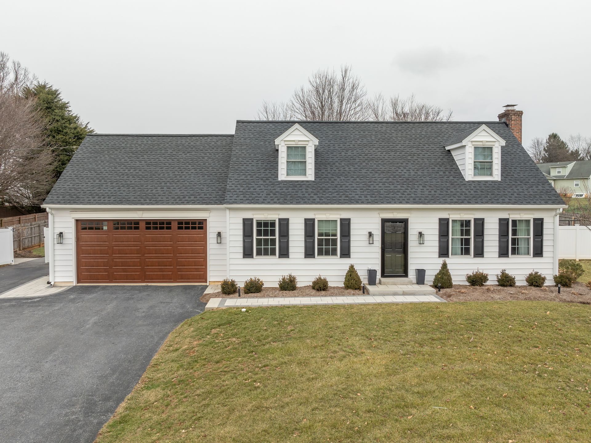 Suburban house with gray roof, white siding, attached wooden garage, and front lawn